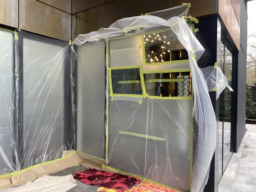 Wraparound main-floor windows of a large home sealed off with plastic sheeting before polishing
